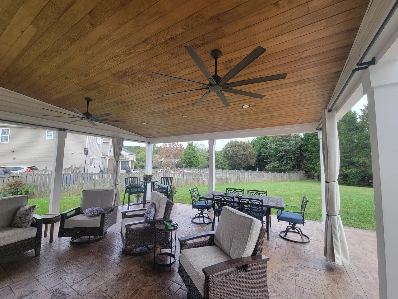 Covered patio with wicker seating, ceiling fans, and a green backyard beyond the open sides
