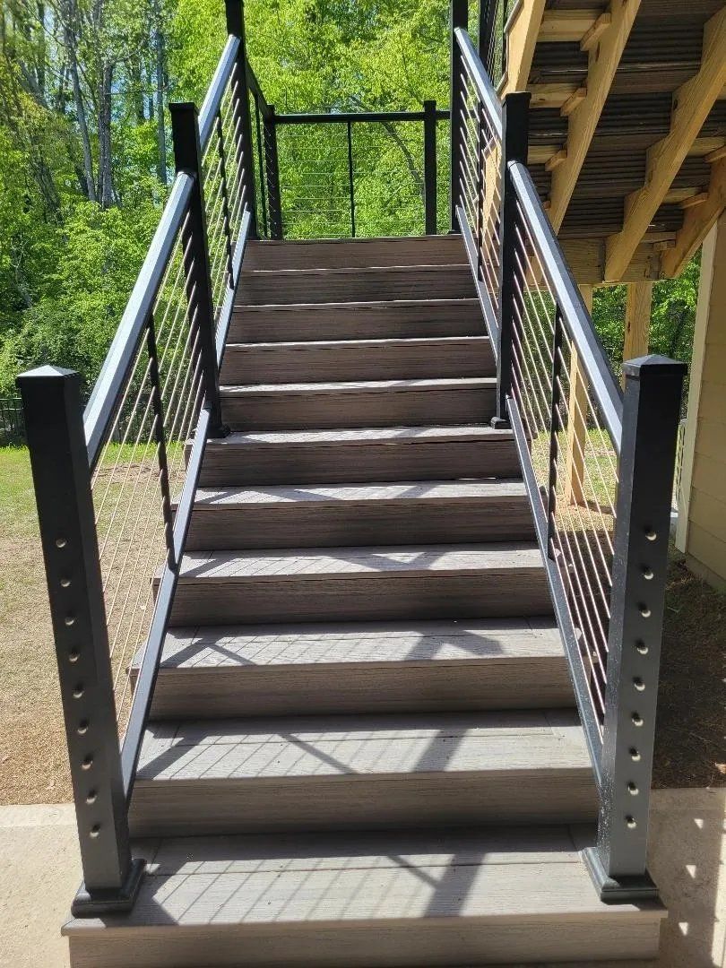 Wooden outdoor staircase with black metal railings leading up to a covered deck amid greenery