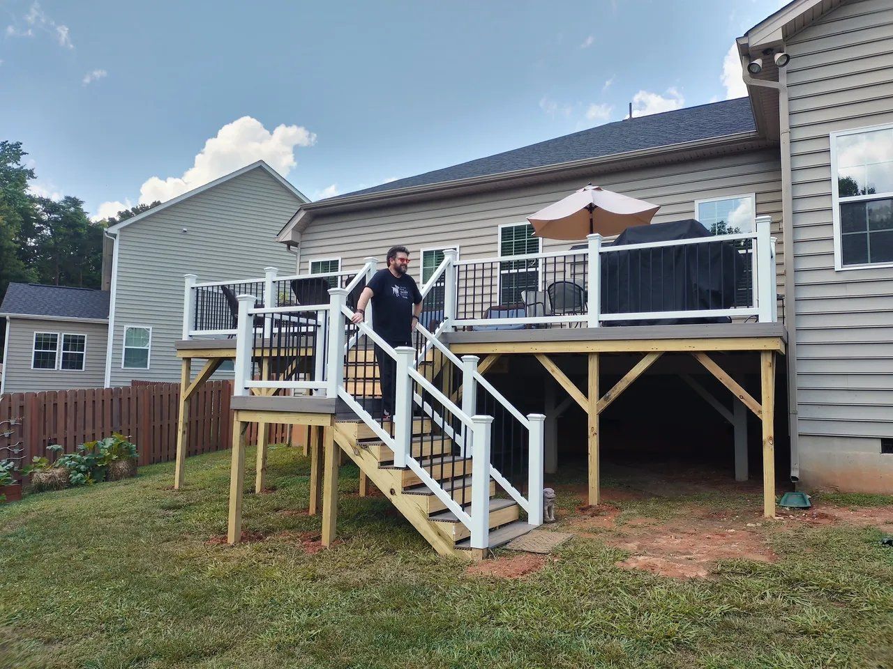 Person standing on a backyard deck with stairs, white railing, and outdoor umbrella attached to a house