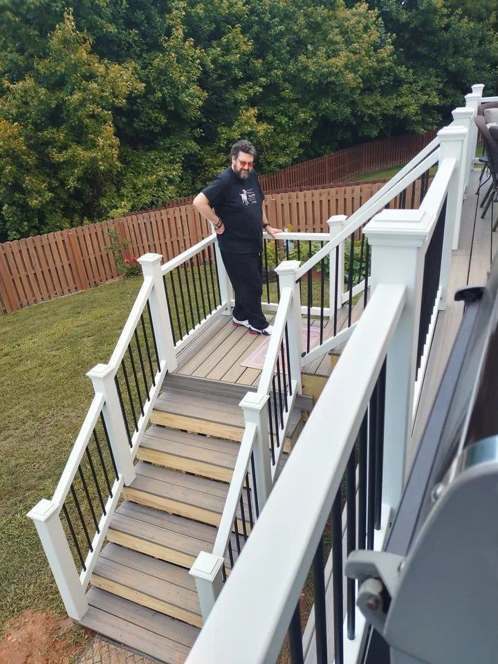 Person standing on outdoor stairs beside a house and wooden fence.