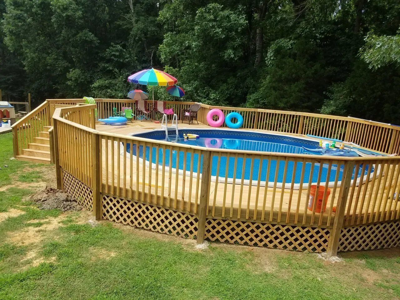 Backyard above-ground pool with wooden deck fencing, rainbow umbrella, and float rings