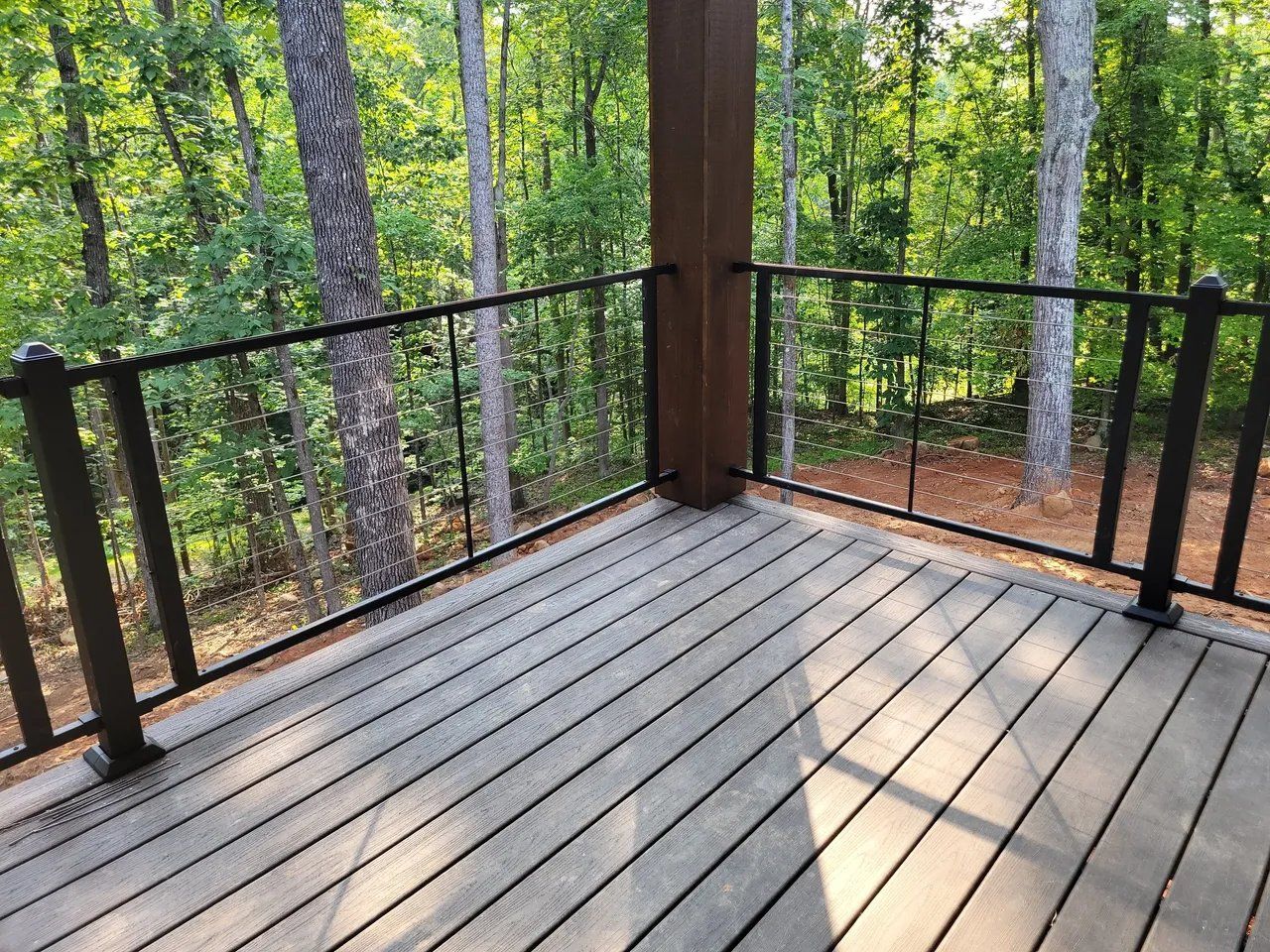 Wooden deck with black railing overlooking a sunlit forest of trees