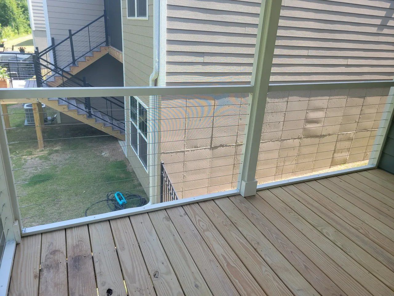 Wooden balcony deck with metal railing overlooking the side of a house and narrow stairway below