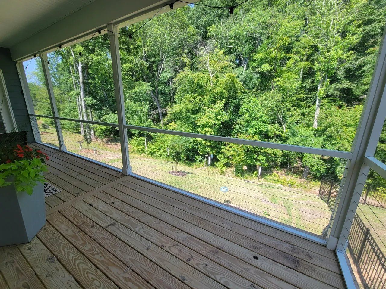 Covered porch with wooden floor, screen railing, and a view of green trees and yard.
