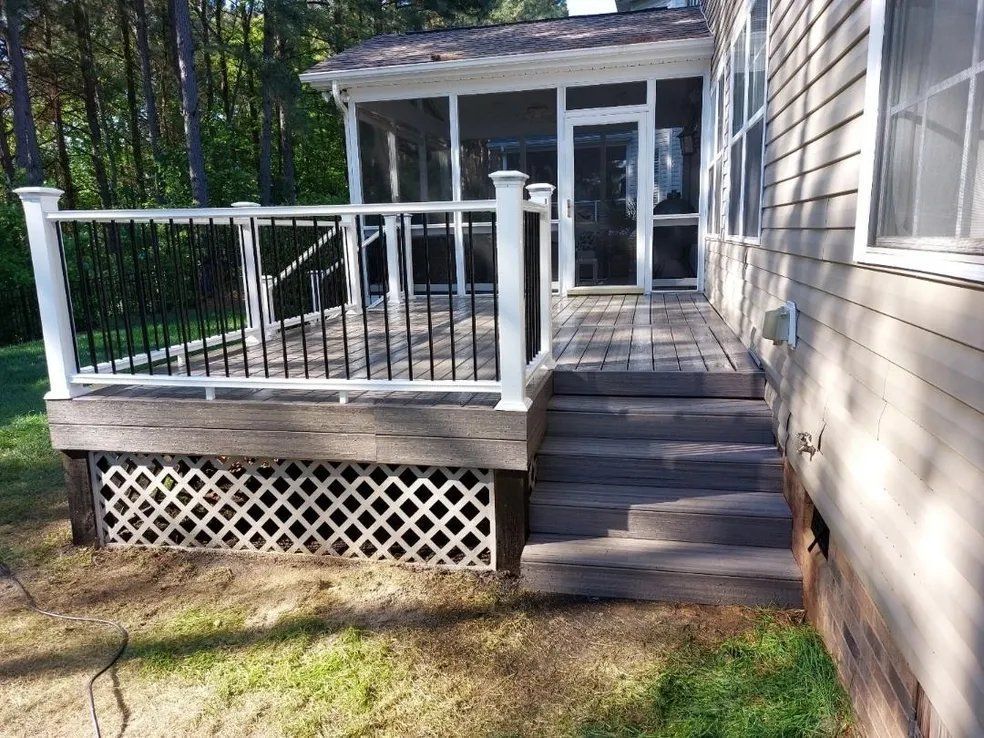 Back deck with white railing, steps, and lattice skirting beside a beige house.