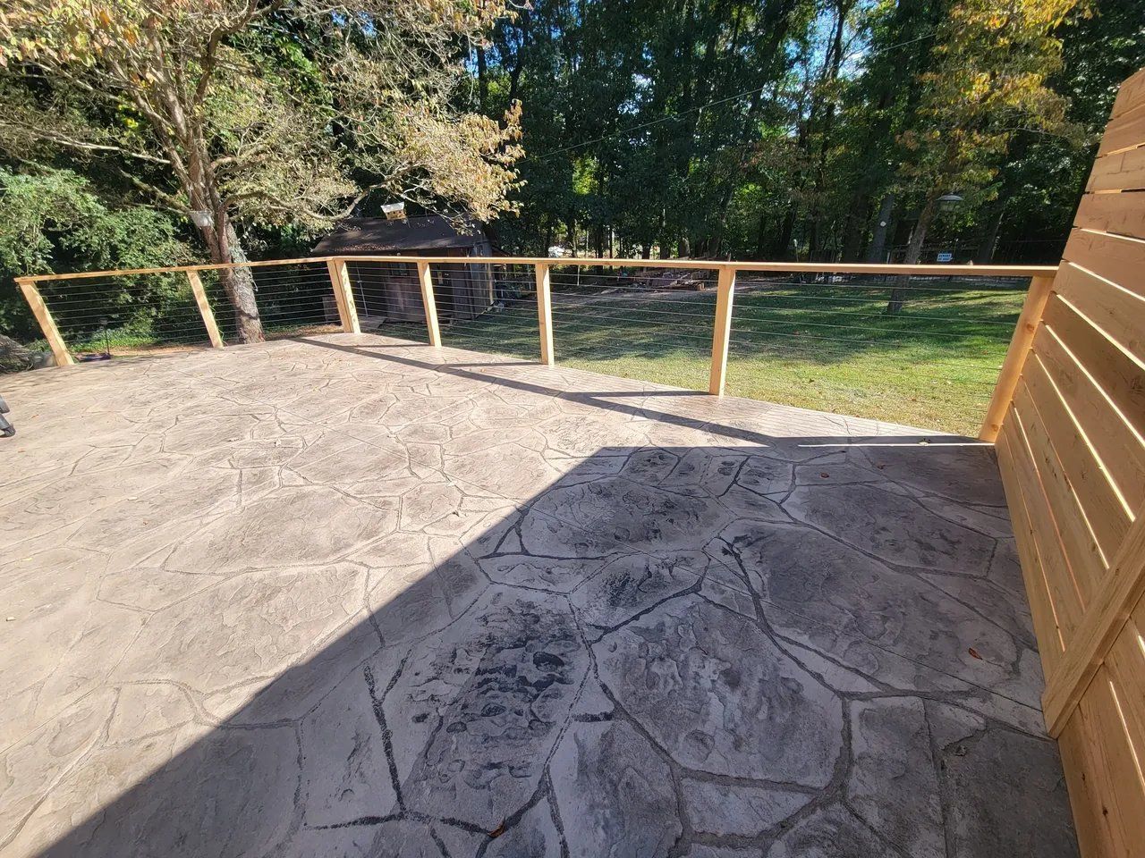 Wooden deck with a railing overlooking a grassy yard and trees in sunlight