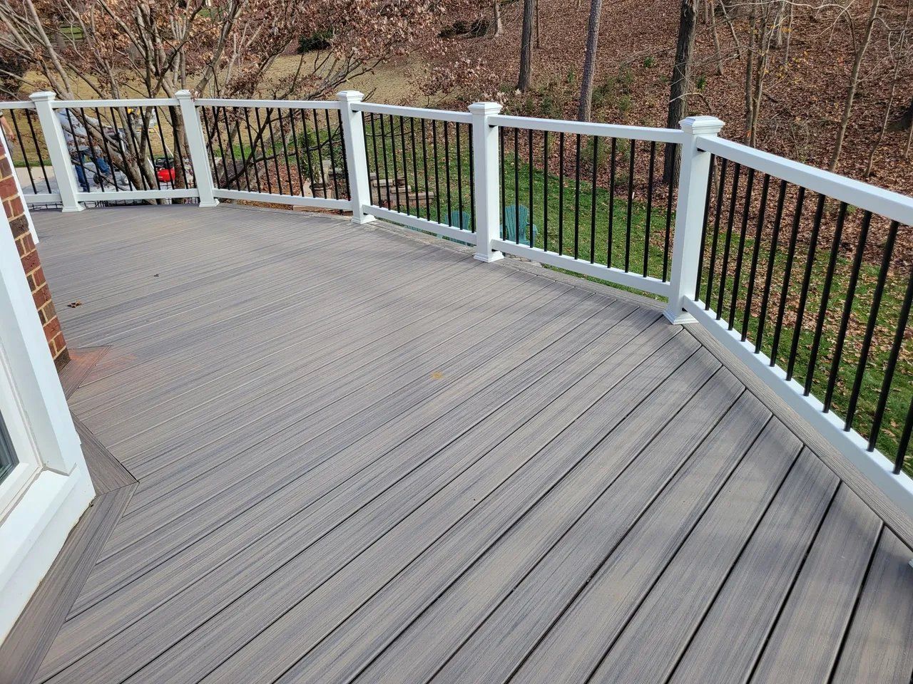 Gray wooden deck with white railings overlooking a grassy yard and trees