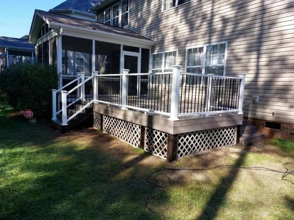 Backyard wooden deck with white railings beside a house, with a small ramp and lattice skirting