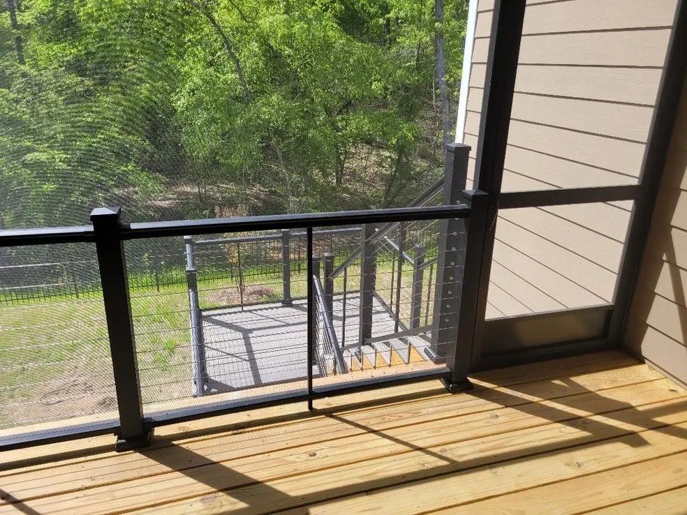 Wooden deck with black railing overlooking a green wooded yard and stone patio below