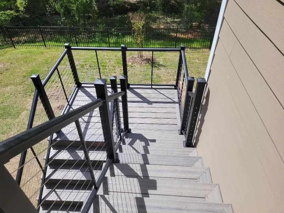 Outdoor wooden deck stairs with black railings beside a beige house, overlooking a grassy yard