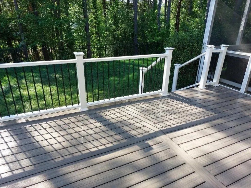 White wooden deck with railing overlooking a green wooded yard in daylight