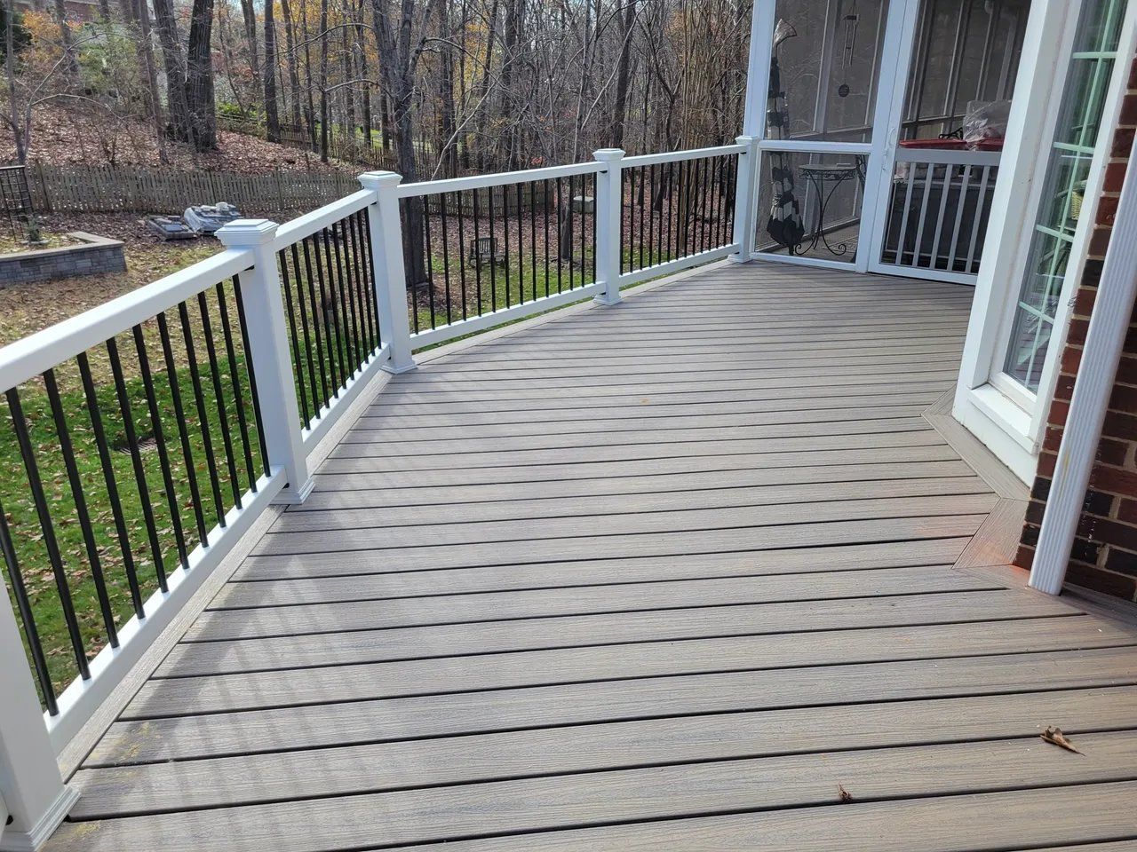 Wooden deck with white railing beside a house, overlooking a wooded yard