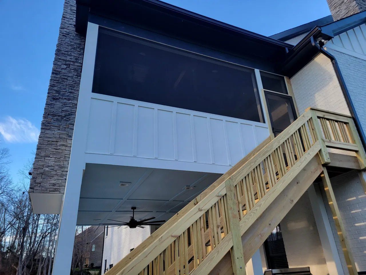 Exterior of a white two-story house with a dark screened porch and wooden stairs at dusk