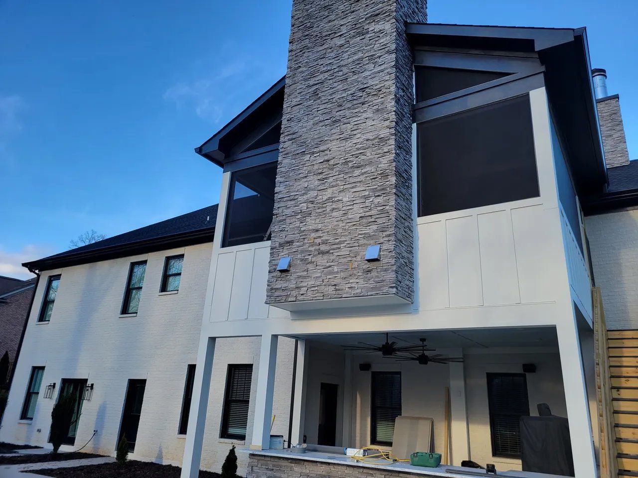 Modern two-story house with white siding, dark roof, and stone-accented central entry.