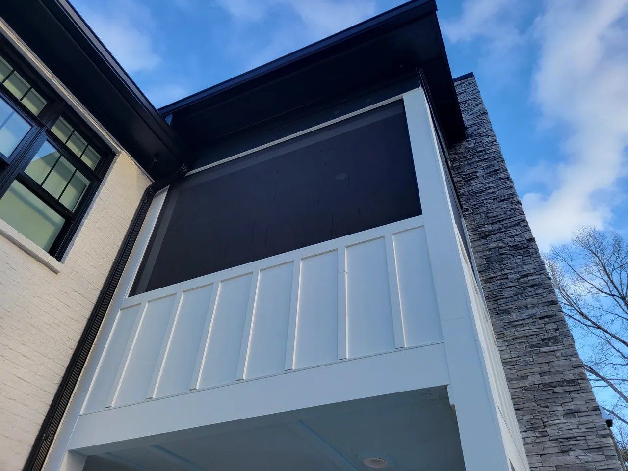 Low-angle view of a modern building facade with white panels, dark window screens, and stone siding.