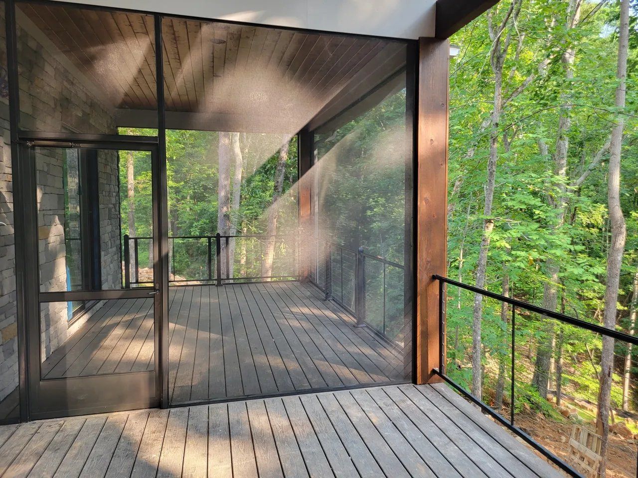 Modern glass-walled deck with wooden floor overlooking a green forest