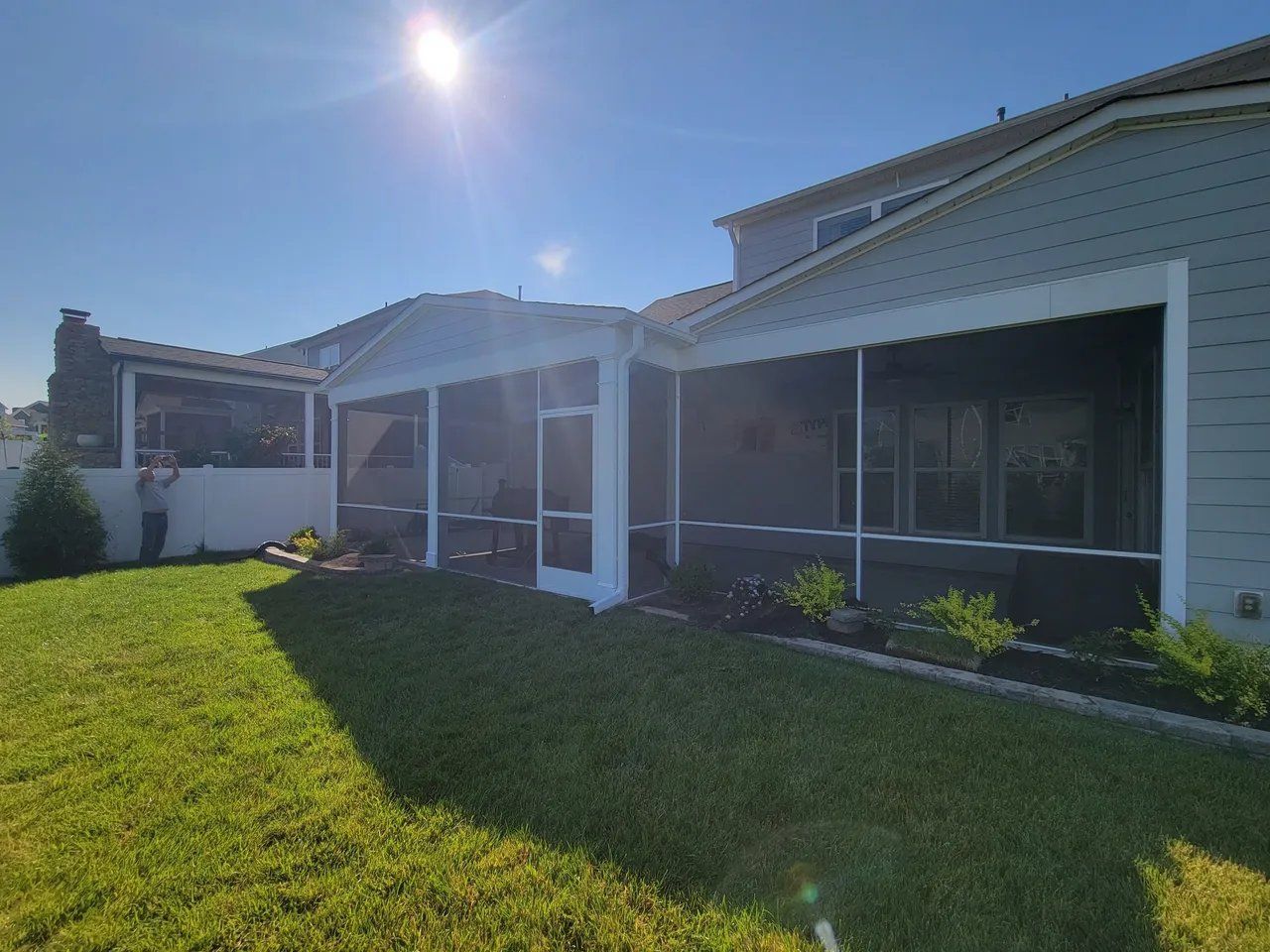 Sunny backyard view of a white house with screened porch and green lawn