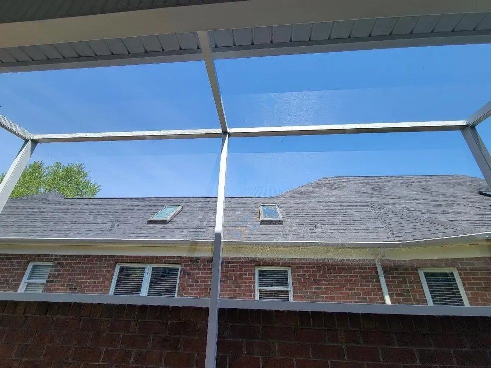 View from a covered patio toward a brick house with gray shingled roof and blue sky