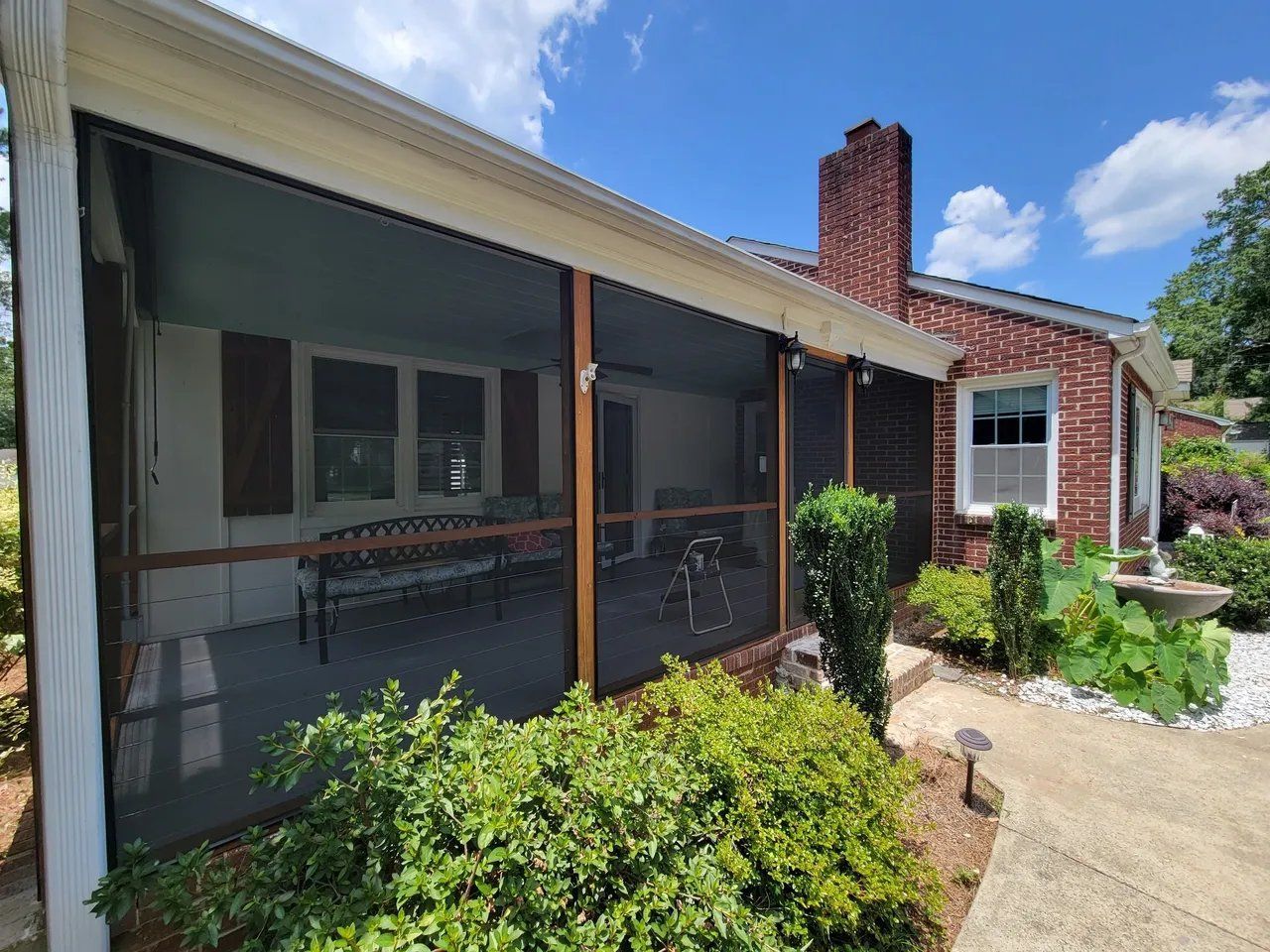 Screened porch on a red-brick house with windows, a brick chimney, and a garden path in front