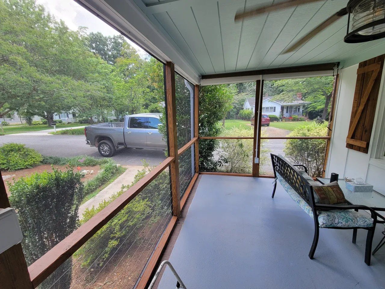 Screened porch with bench overlooking a suburban street and parked gray truck