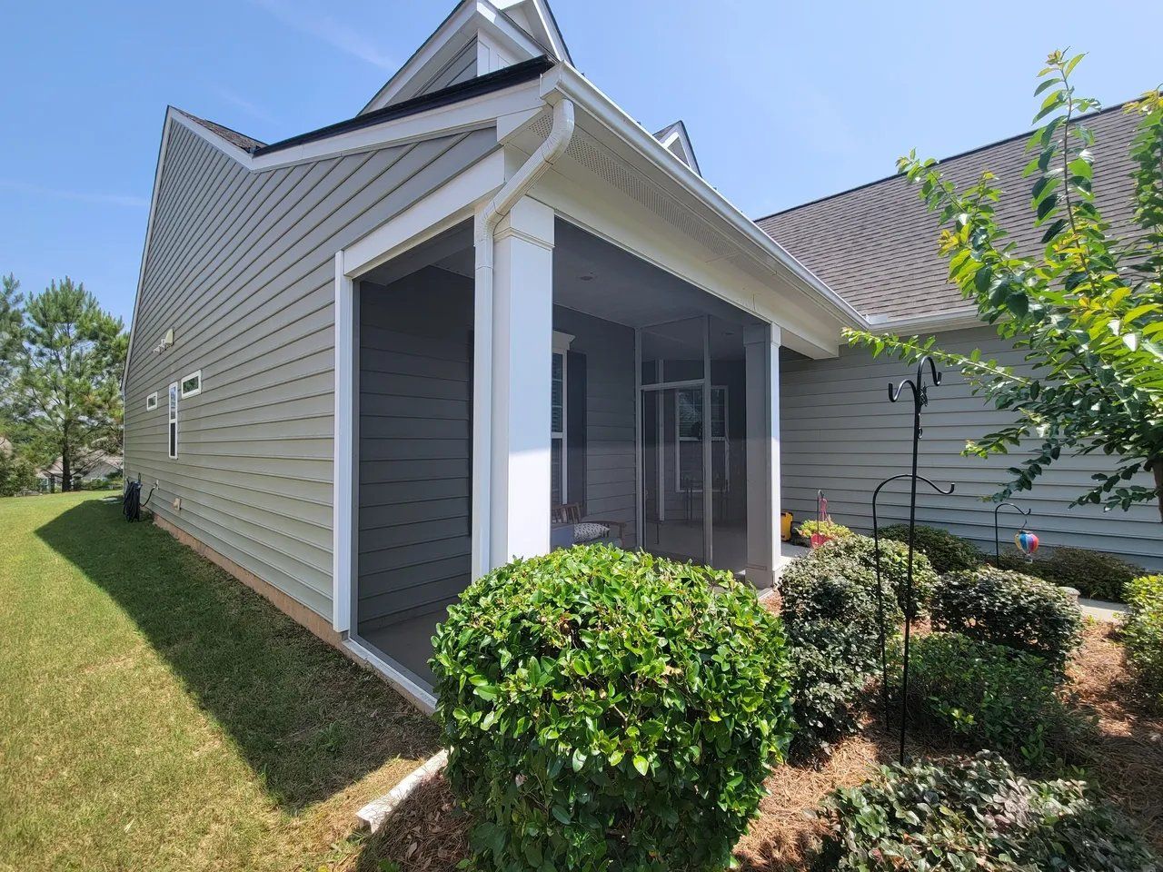 Screened porch entrance on a suburban house with gray siding and landscaped yard