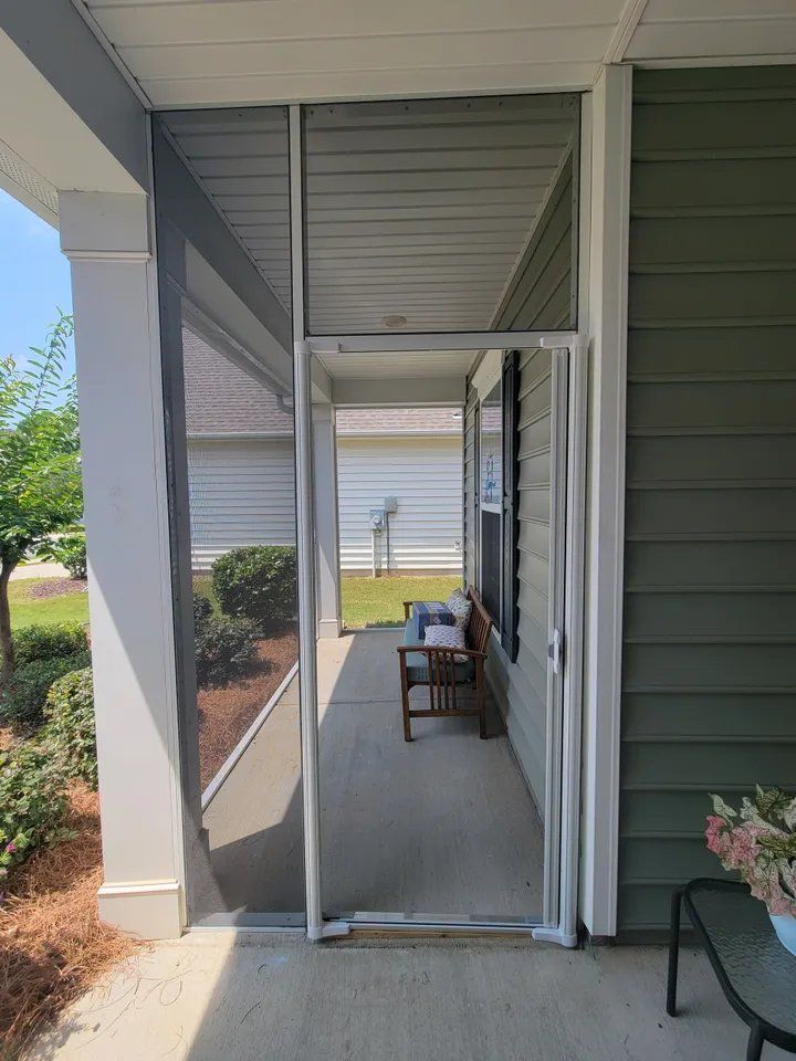 Covered front porch with white columns, green siding, and two chairs along a narrow walkway.