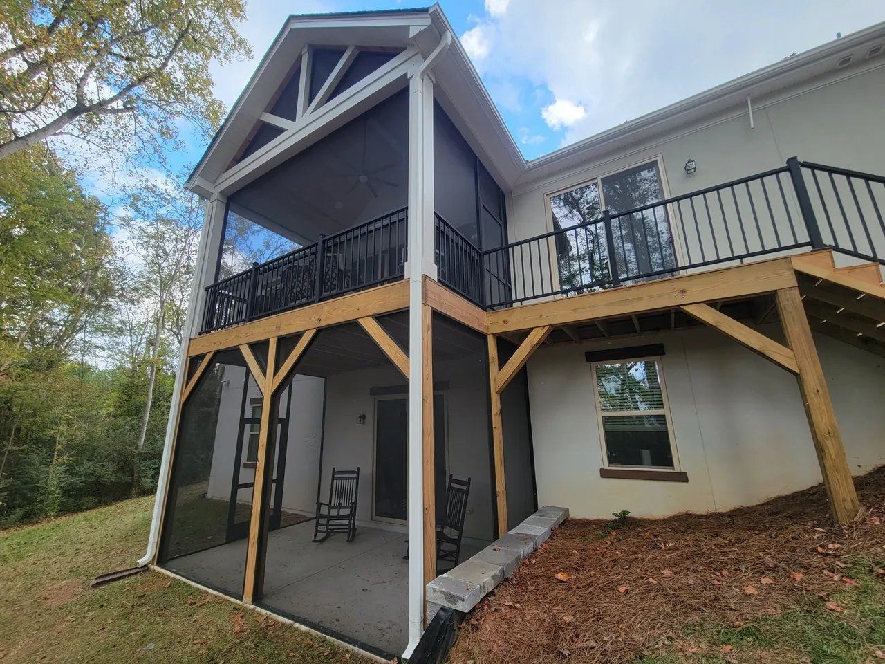 Gray house with a raised deck and wooden support posts, viewed from the backyard under a cloudy sky