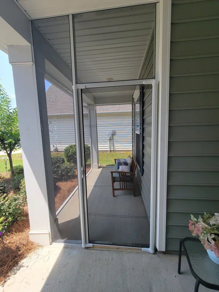 Front porch with a screened door, gray siding, white columns, and outdoor chairs in sunlight