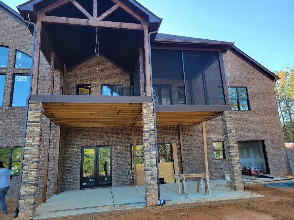 Brick house under construction with two covered porches and exposed framing