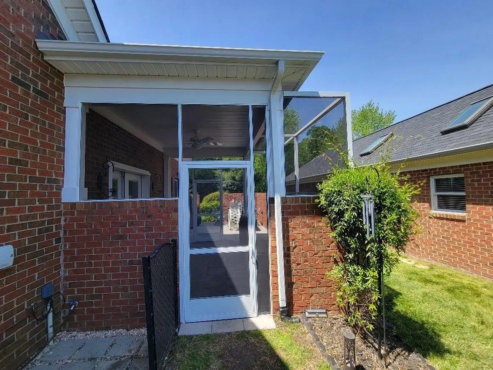 Brick house side entrance with a white door, screened porch, and open gate beside a grassy yard.
