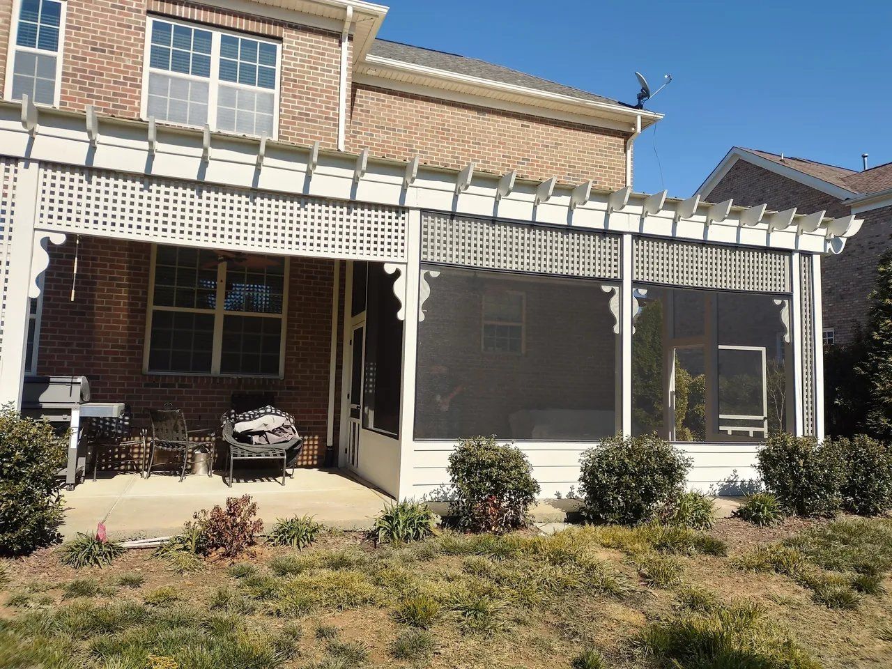 Brick house with white pergola over a covered patio and screened porch, fronted by a small yard.