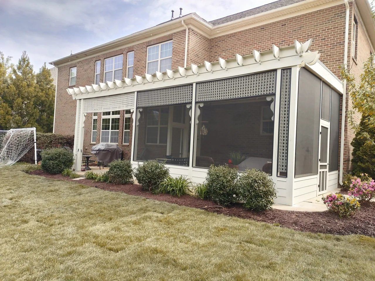 Two-story brick house with a screened porch and white trim, viewed from a grassy yard.