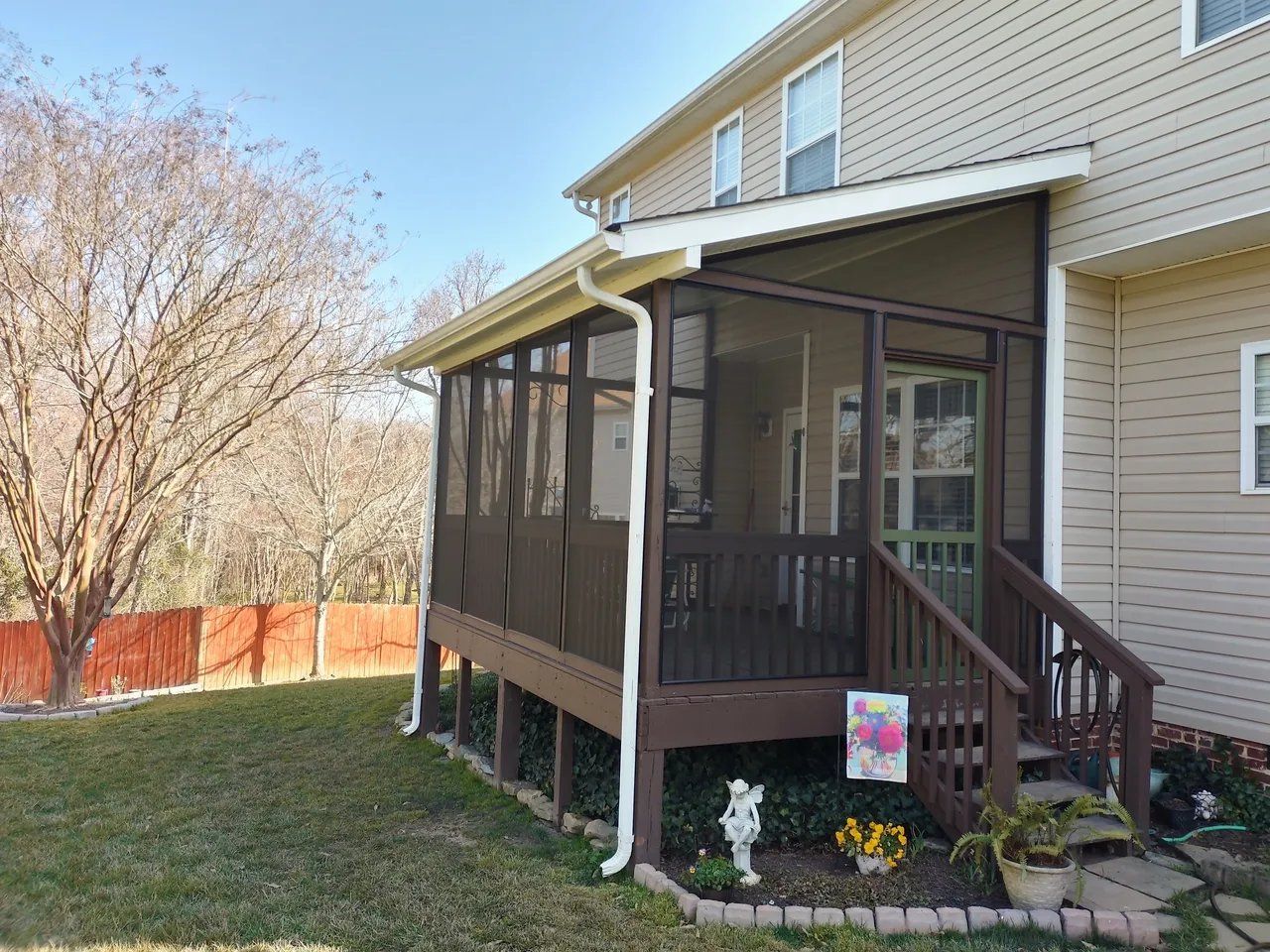 Screened porch attached to a beige house with stairs, flowers, and a grassy yard.