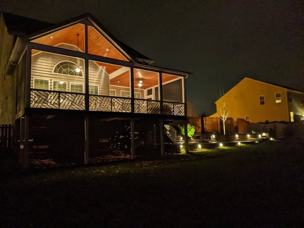 Lit house porch at night with warm lights and a walkway in a dark yard