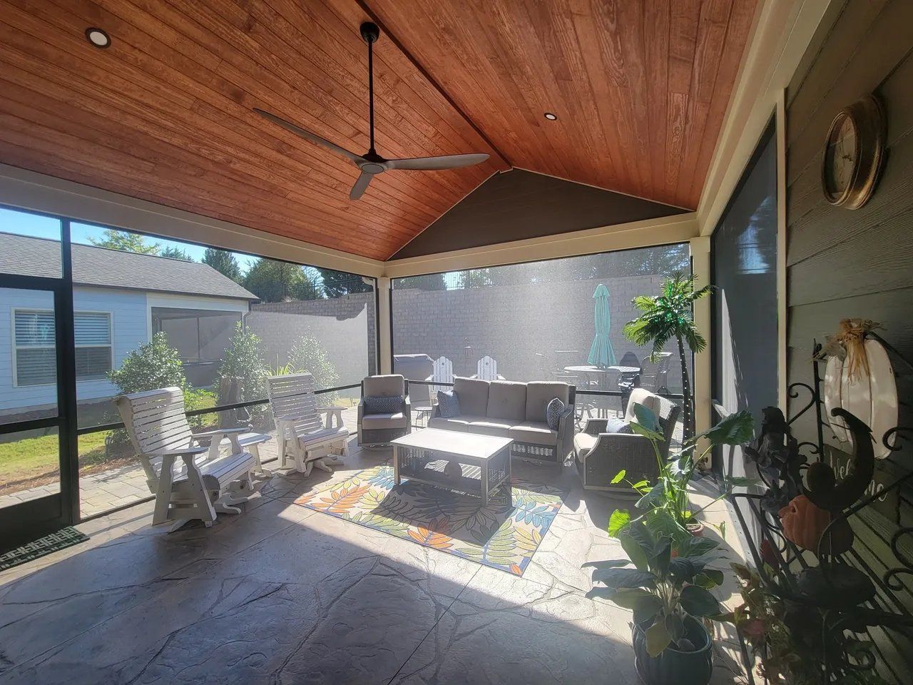 Covered patio with wood ceiling, ceiling fan, seating, and potted plants in bright sunlight