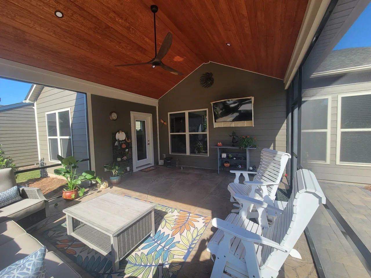 Covered patio with wicker seating, coffee table, and open doors facing a fenced backyard.