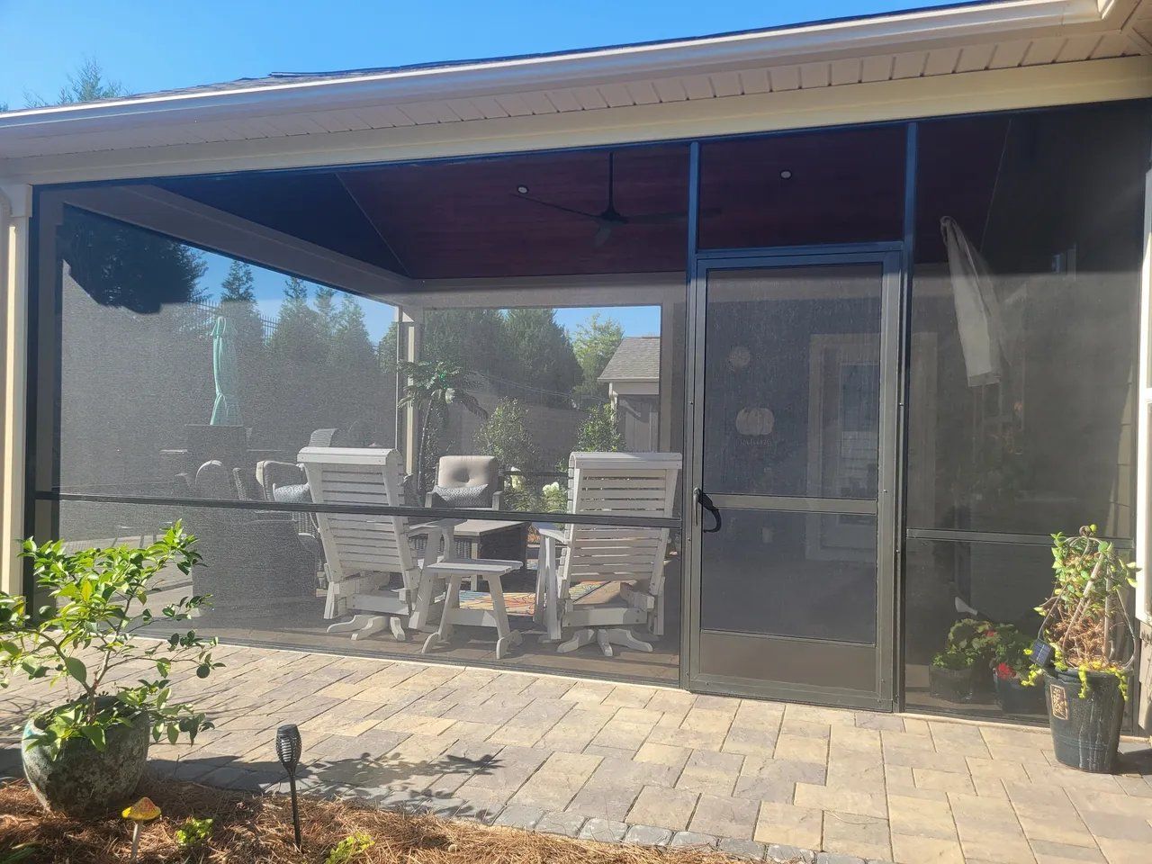Patio with screen enclosure, outdoor dining table, chairs, and potted plants beside a house