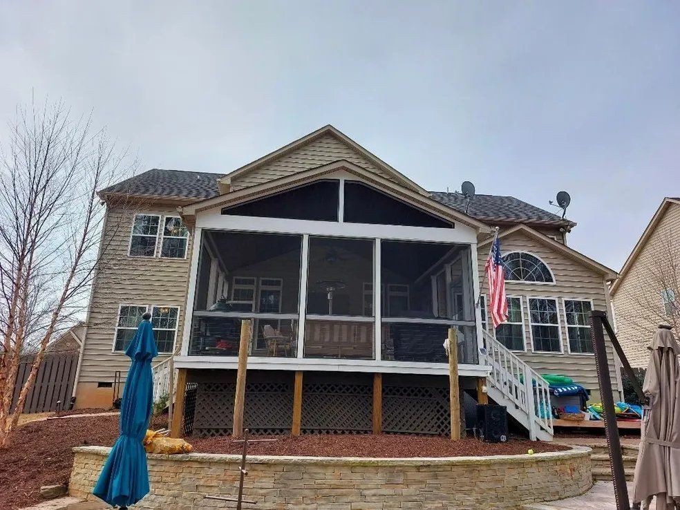 Backyard view of a two-story house with a covered porch, blue umbrella, and patio chairs