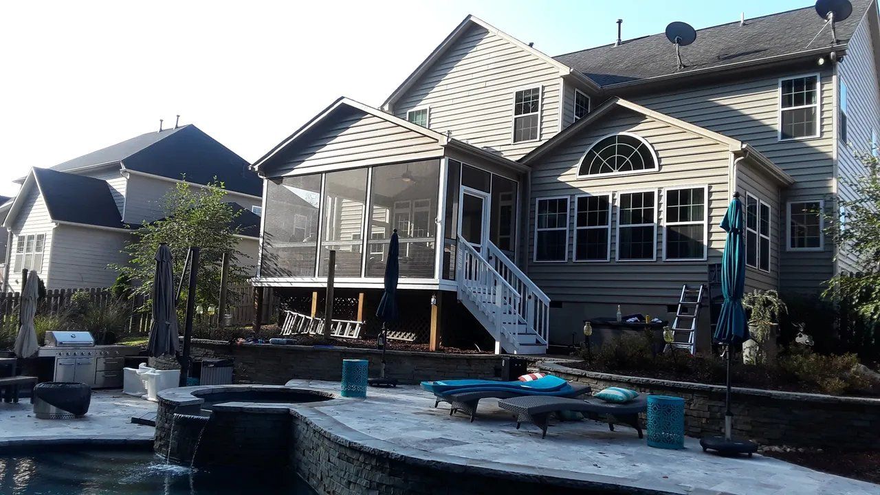 Backyard patio with a pool and screened porch on a beige house, lit by bright sunlight