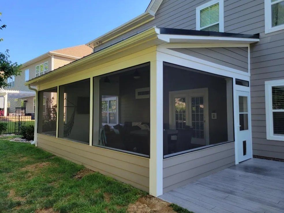 Screened porch with gray siding, tan trim, large windows, and a wooden deck beside a house