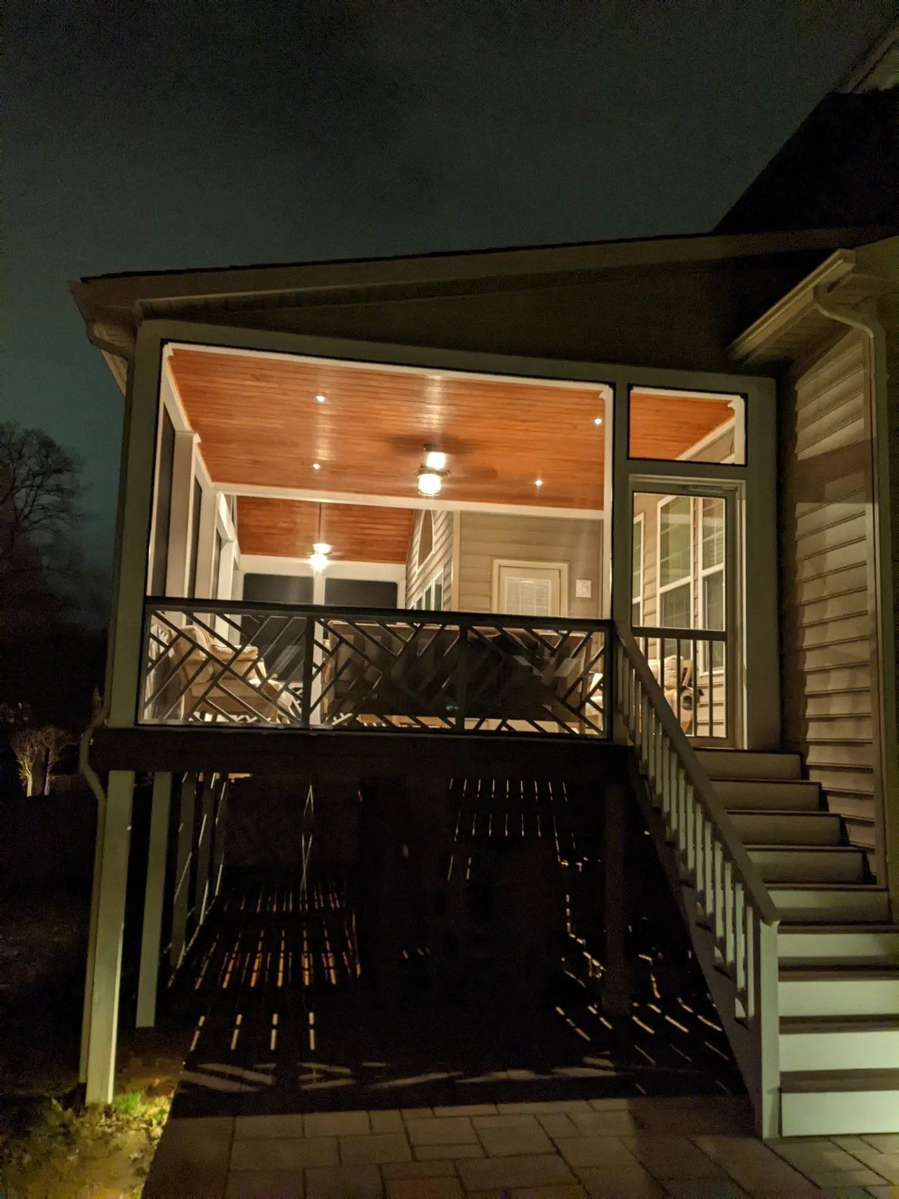 Lit porch and deck at night with stairs leading up to a screened entry.