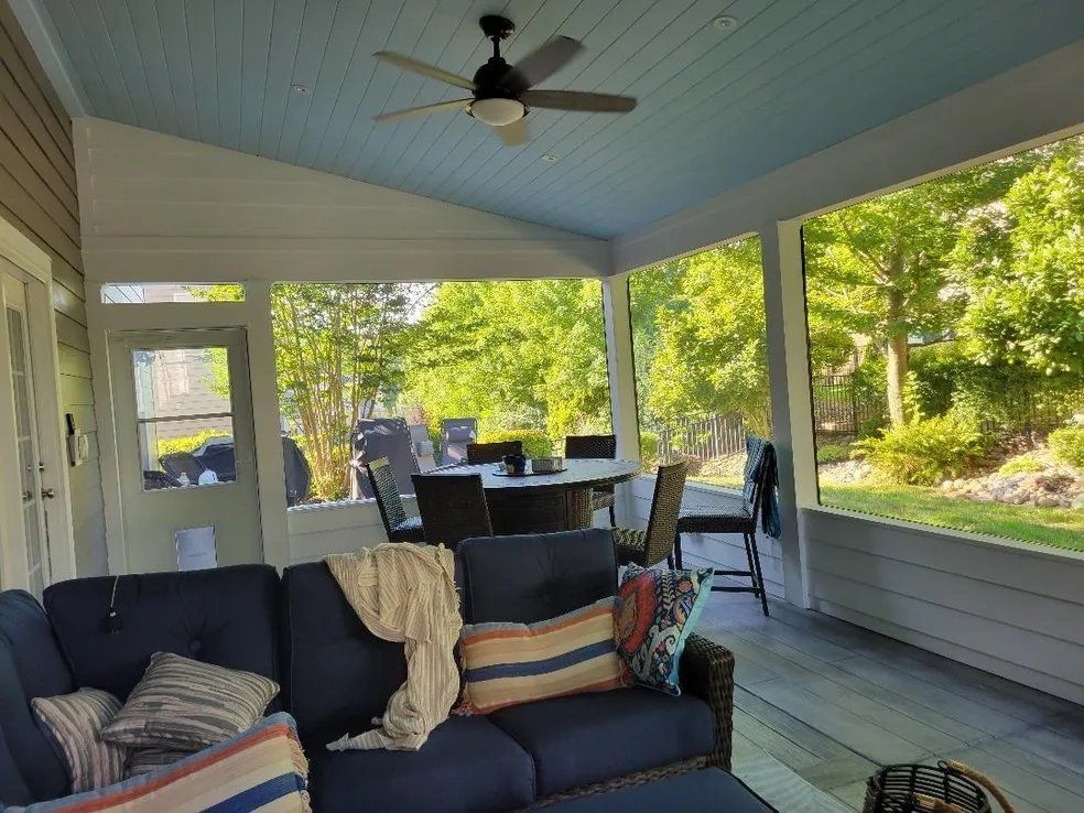 Covered porch with sofa, dining table, ceiling fan, and views of a green backyard