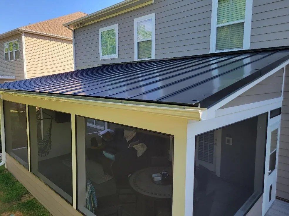 Back porch with screened enclosure and dark metal roof attached to a gray house.