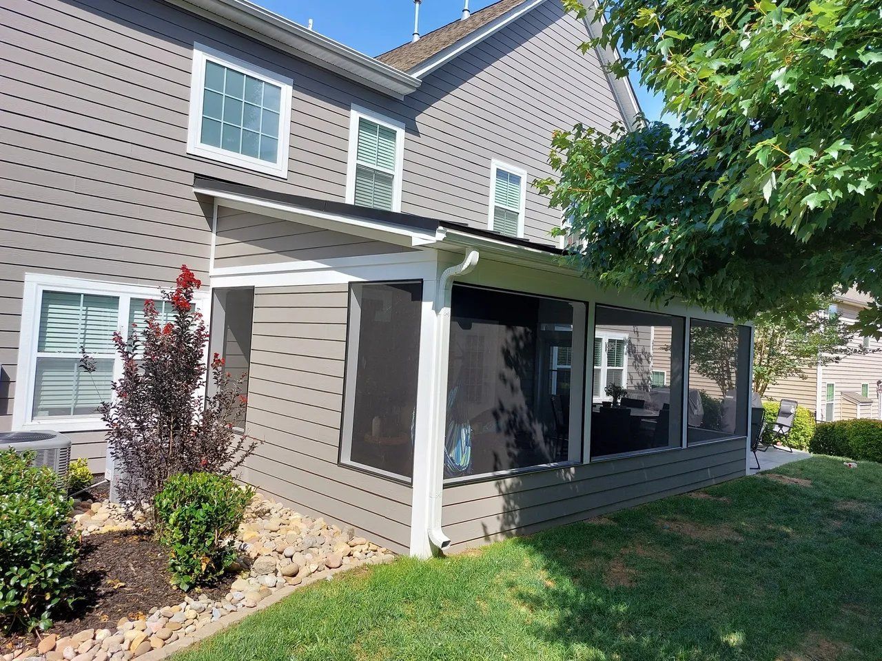Brown two-story house with a covered back porch, white trim, and a grassy yard.