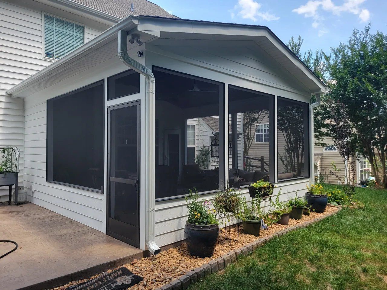 Screened porch on a white house with black trim, potted plants, and a concrete patio