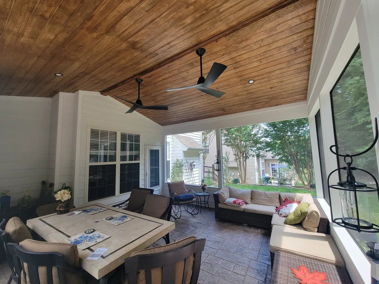Covered outdoor patio with dining table, cushioned seating, ceiling fans, and a view of the yard
