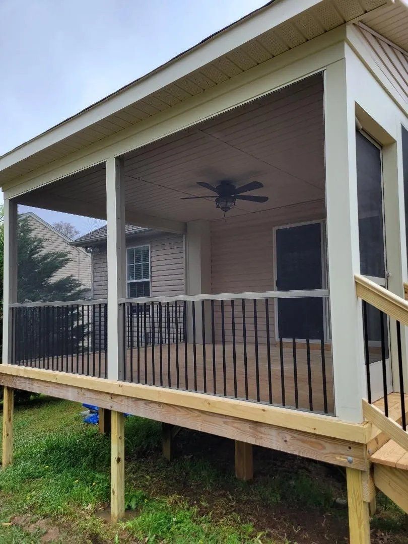 Covered porch with a ceiling fan and black railing on a raised house exterior.