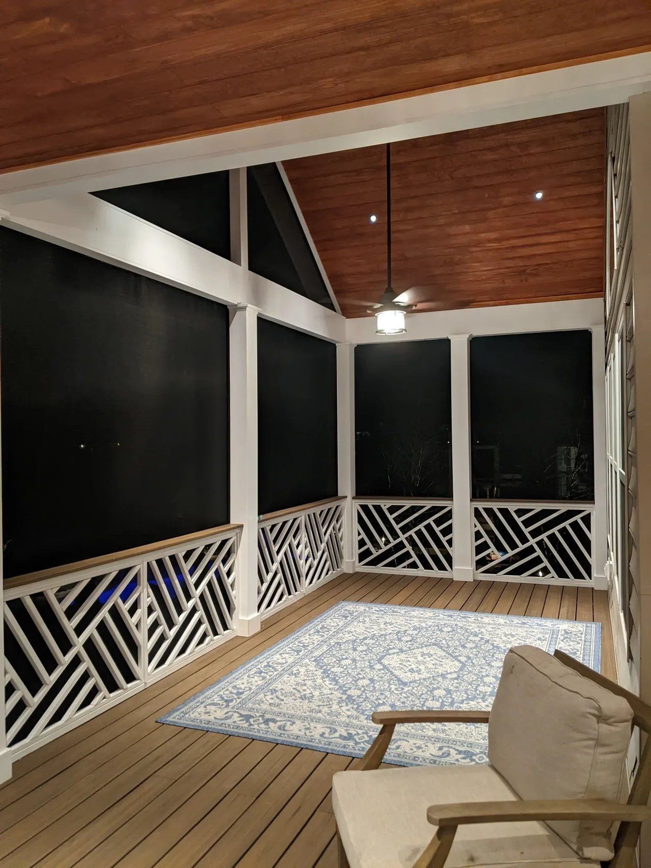 Covered porch with white railings, wood ceiling, rug, and cushioned chair at night