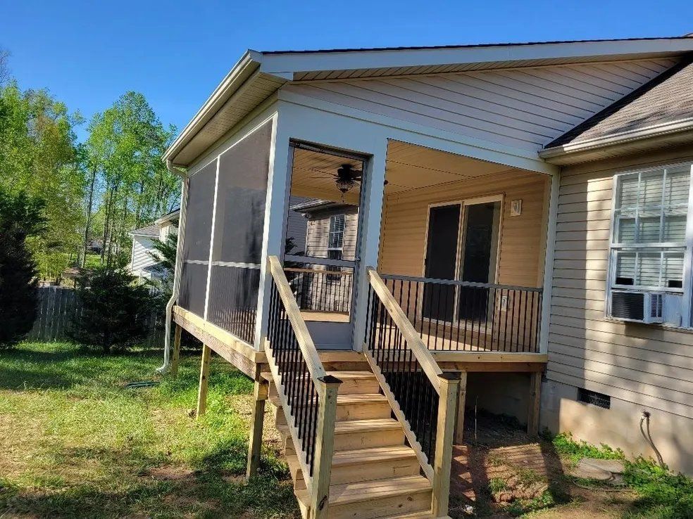 Back porch ramp and stairs on a beige house, with a small deck and railing in a grassy yard.