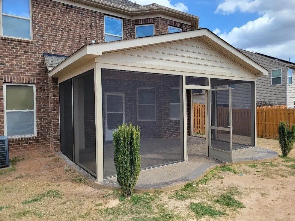 Screened-in back patio attached to a brick house with a small concrete slab and dry yard.